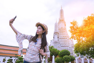 Portrait of young woman photographing against sky