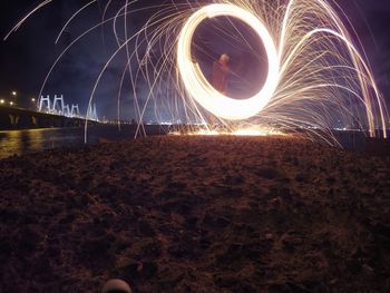 Man spinning wire wool on rock formation at sea shore during night