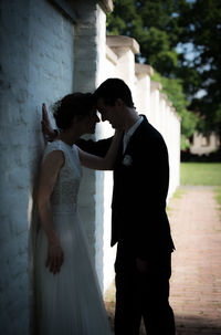 Side view of romantic bride and groom standing by wall on footpath