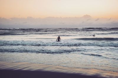 Silhouette man with surfboard on beach against sky during sunset