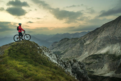 Biker with bicycle on top of mountain under cloudy sky