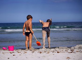 Rear view of shirtless brothers playing at sandy beach