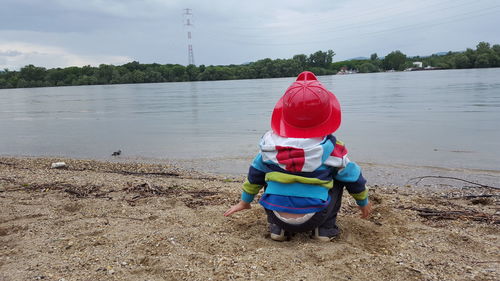 Rear view of child crouching at lakeshore