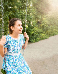 Blue-eyed girl rides on a swing in the park against the background of trees or on the playground