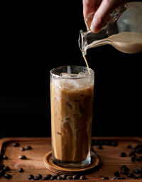 Cropped hand pouring coffee in drinking glass on table against black background