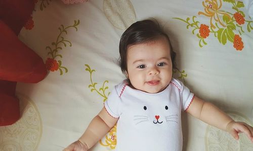 Portrait of cute baby girl lying on bed at home