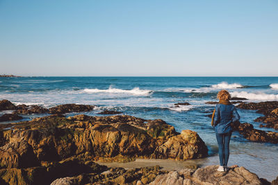 Woman standing on beach against clear blue sky