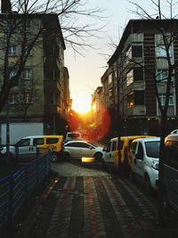 Cars on city street amidst buildings against sky at sunset