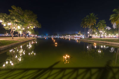 Illuminated city by river against sky at night