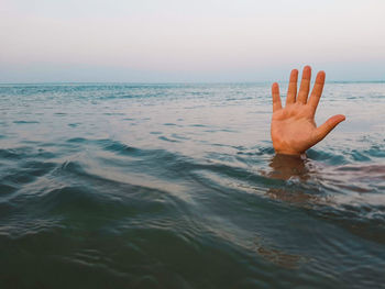 Close-up of hand in sea against sky