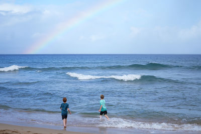 Young boys playing in the waves with a rainbow over the ocean on ka'anapali beach in hawaii. 