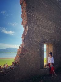 Full length of man sitting at shore against sky