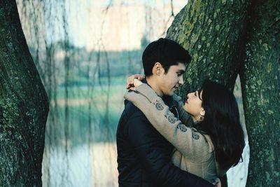 Close-up of smiling couple embracing while standing against trees