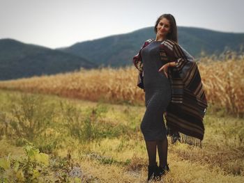 Portrait of young woman standing on grassy field against sky