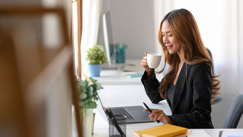 Businesswoman drinking coffee while working at office