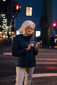 Smiling woman texting through smart phone while standing in illuminated city at night