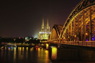 Illuminated bridge over river against sky at night