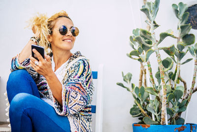 Woman wearing sunglasses looking away while sitting against wall