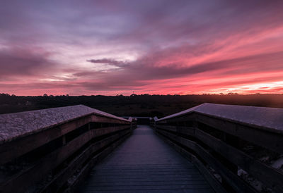 Footbridge against cloudy sky during sunset