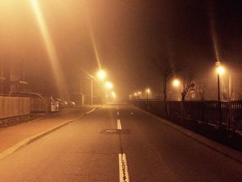 Empty road along illuminated street lights at night