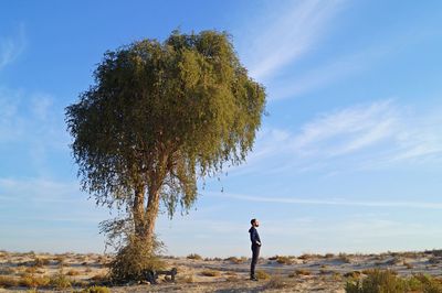 Full length side view of man standing by bare tree against blue sky