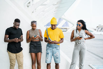 Young black people in stylish clothes standing in urban area and messaging on social media via smartphones