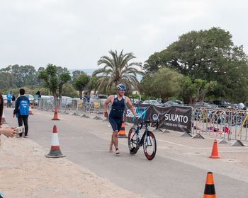 Man running with bicycle on street against sky