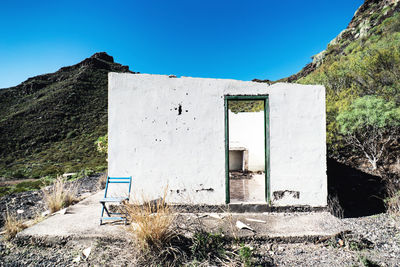 Abandoned building on field against clear blue sky