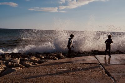 Water splashing on rocks by sea against sky