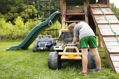Rear view of young boy pretending to fix engine on toy ride-on car
