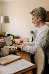 Side view of lesbian businesswoman using laptop sitting at dining table