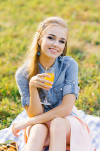 Young woman in a blue denim shirt and pink skirt in the garden at a picnic holding a glass of juice