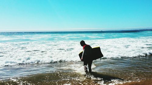 Rear view of man standing on beach against clear sky