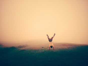 Rear view of man practicing handstand on grassy field during foggy weather