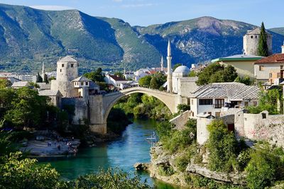 Bridge over river by houses and mountains against sky