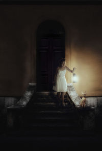 Girl holding old-fashioned lantern by sphynx hairless cat on steps at night