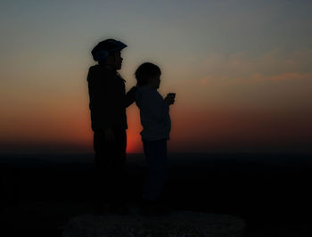 Silhouette couple standing against orange sky during sunset