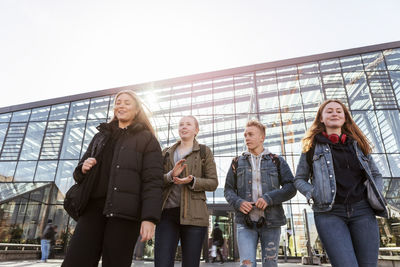 Low angle view of teenage friends walking against railroad station in city