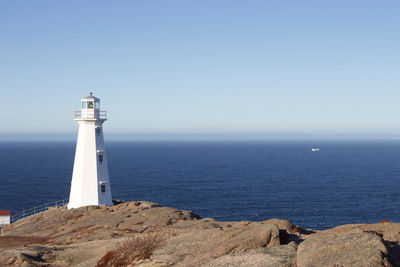 Lighthouse by sea against clear sky