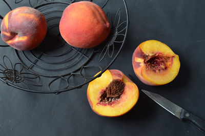 Halved peach and knife next to wire basket with whole peaches