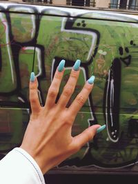 Cropped hand of woman with painted fingernails against graffiti wall