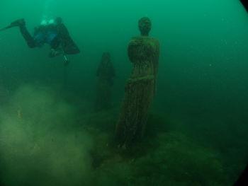 Person scuba diving by statues in sea