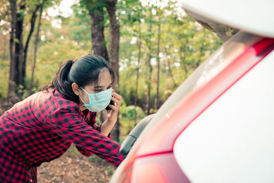 Rear view of woman holding umbrella against trees