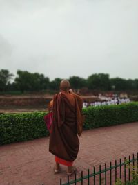 Rear view of monk wearing traditional clothing standing on footpath