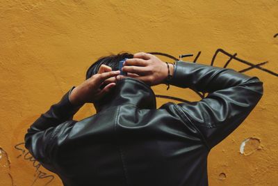 Rear view of man wearing leather jacket against wall