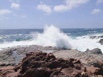 Waves breaking on shore against sky