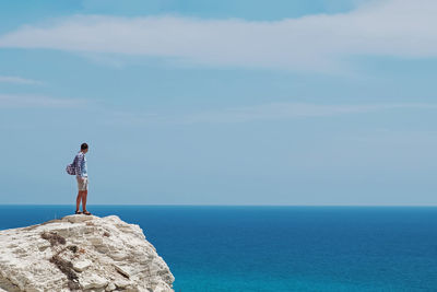 Rear view of woman standing on rock by sea against sky