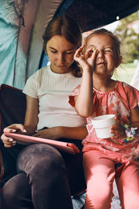 Two girls sisters spending family time in a tent on camping. children using tablet playing games