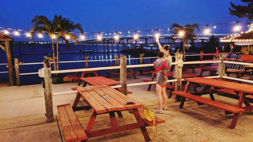 Empty chairs and tables at restaurant against sky at night