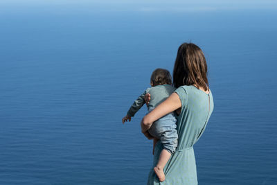 Rear view of woman with daughter standing against blue sky